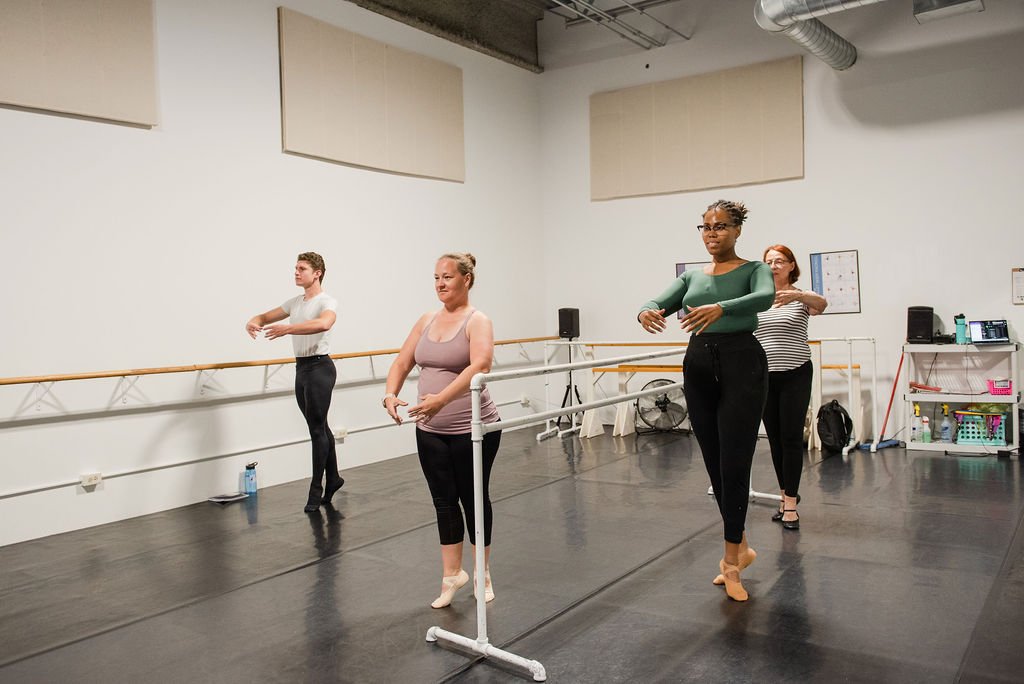Four ballet dancers practicing at the barre in a dance studio.