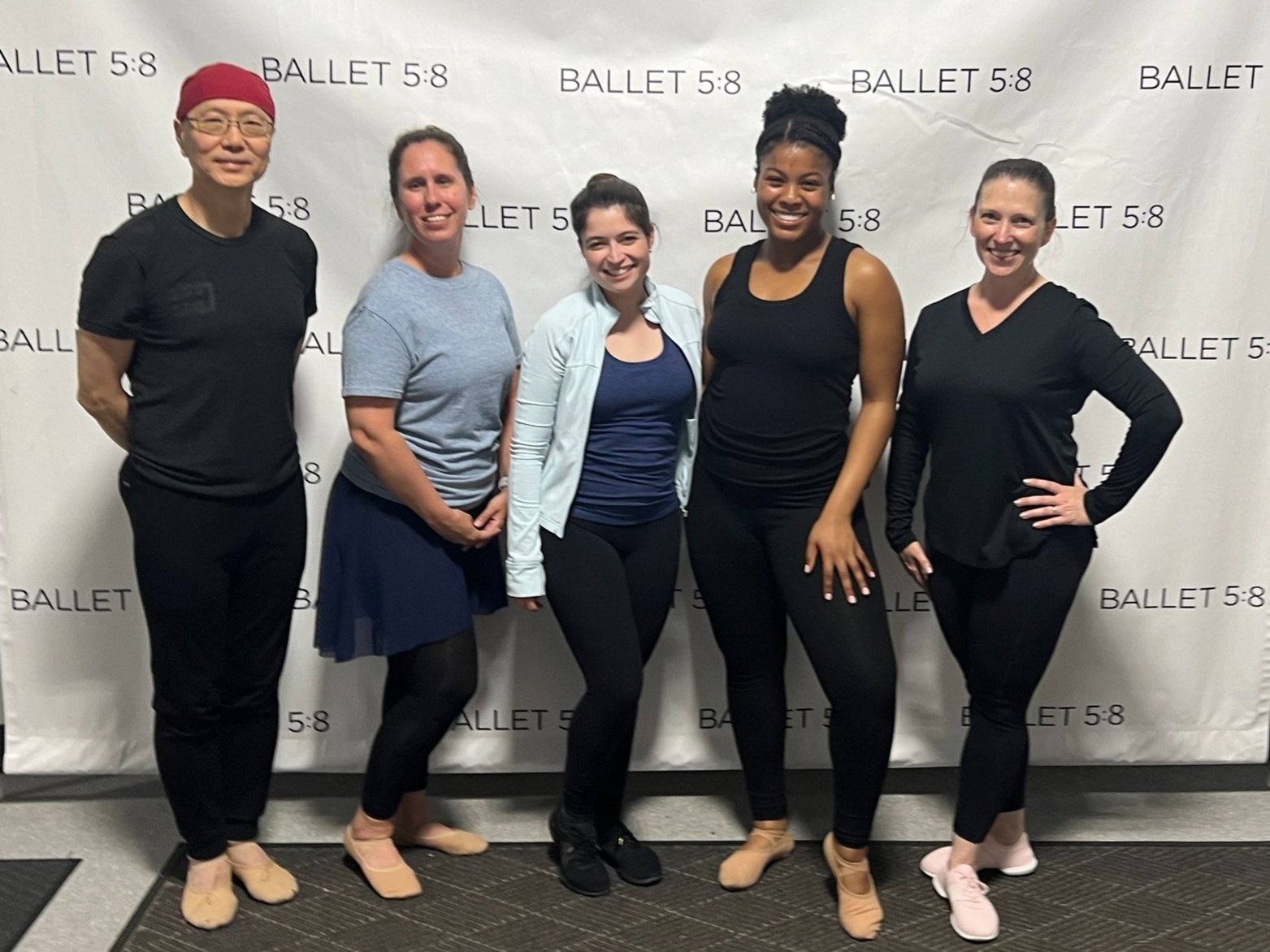 Five ballet dancers standing in front of a backdrop with