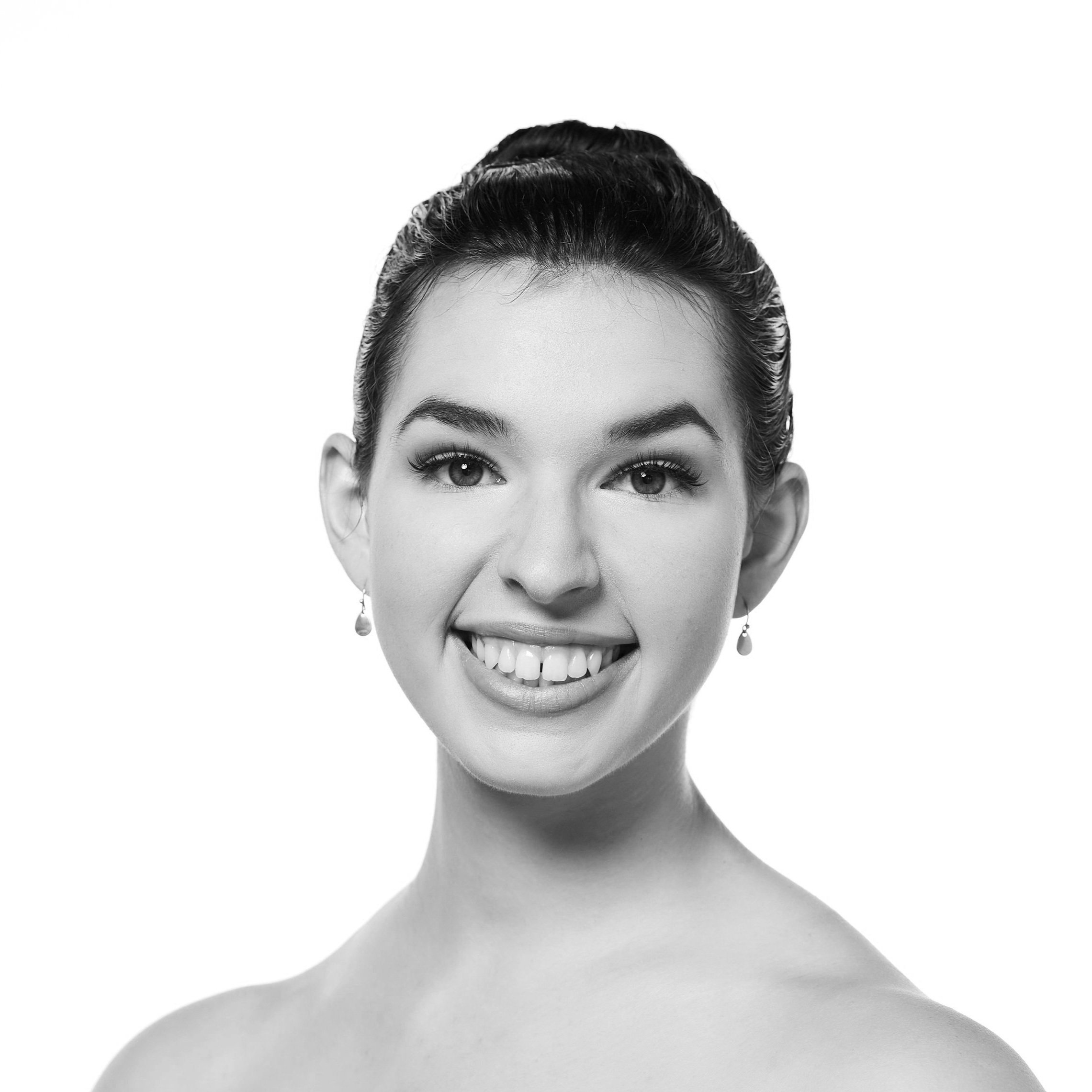 Black and white portrait of a smiling young woman with hair in an updo, wearing earrings, and showing her teeth.